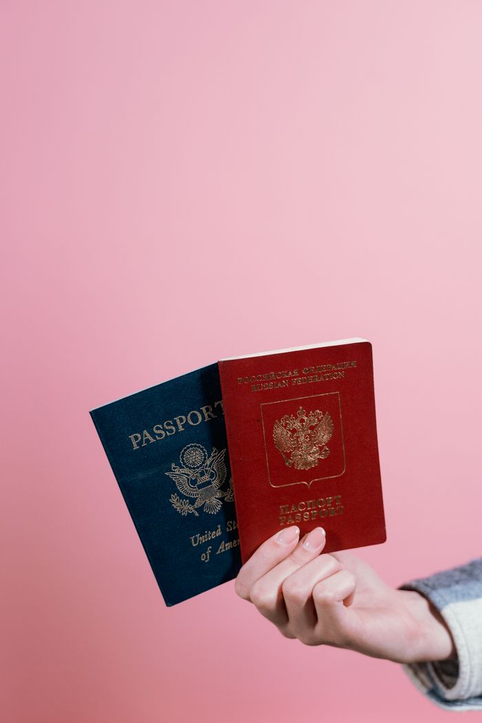 About Close-up of two passports held by a hand against a pink background.